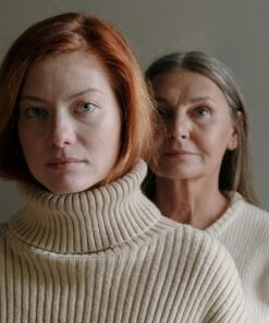 A serene portrait of a mother and daughter in cozy sweaters against a gray background.